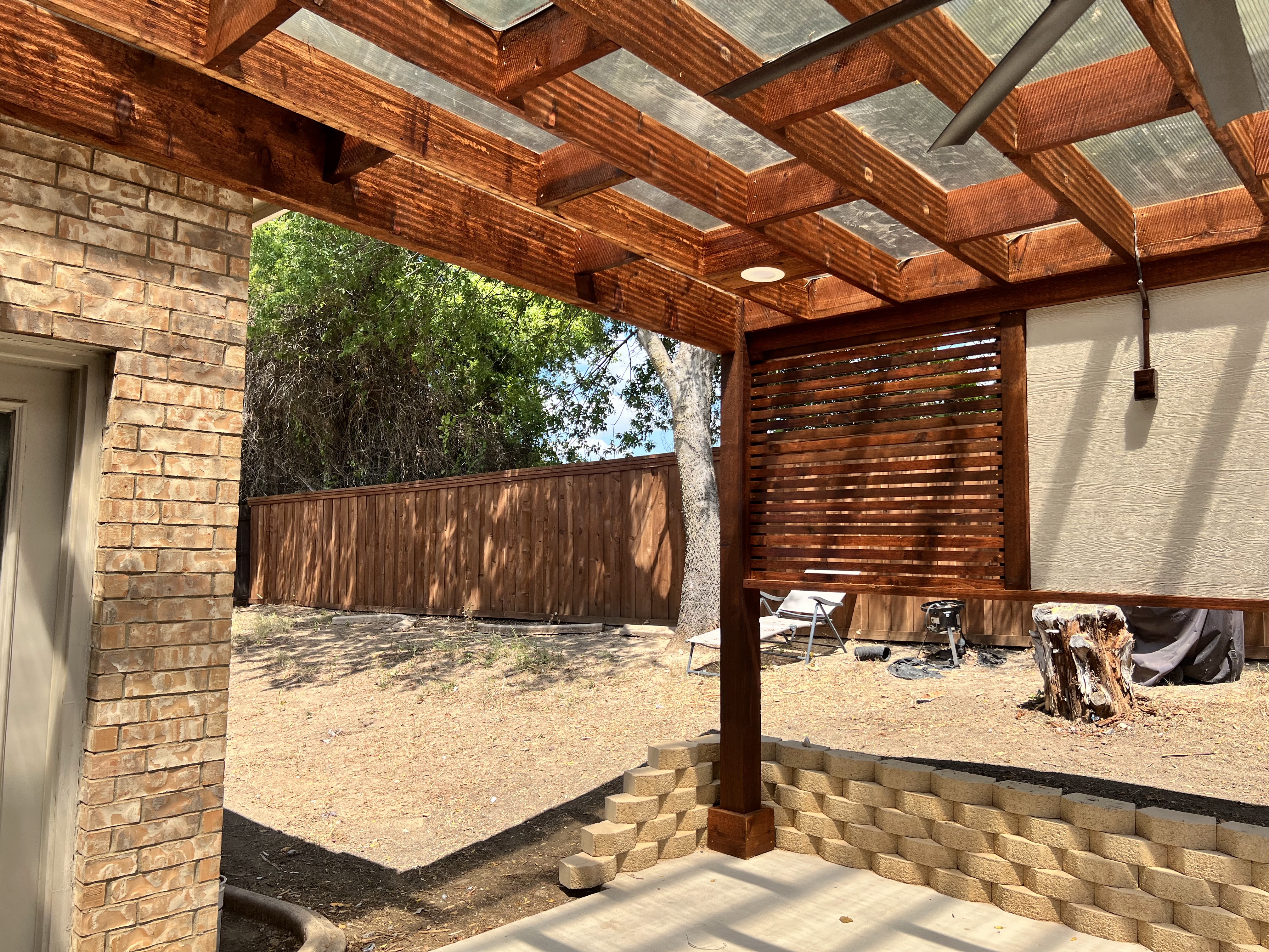 A patio with a custom wooden pergola and a fan, designed by an Outdoor Living Specialist.