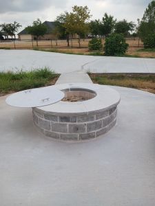 An outdoor fire pit sitting on a concrete slab, perfect for creating a cozy ambiance and enhancing outdoor living spaces in parks or homes.