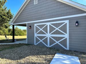 A gray barn with a white door, custom-built by a Home Additions and Custom Home Builder specialist.
